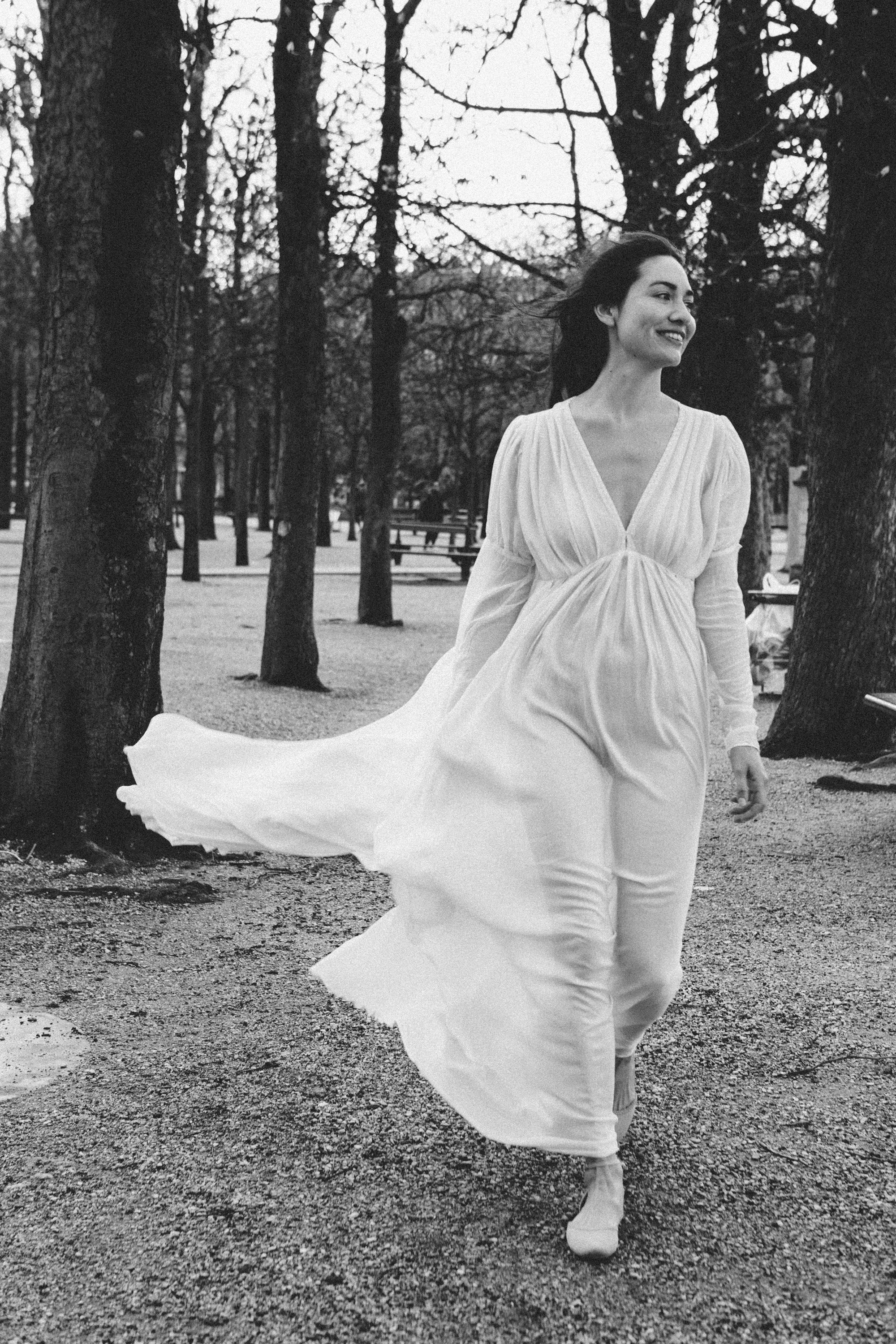 Black and white portrait of a woman in a flowing white dress in a park, film noir style photography by Carla Coulson