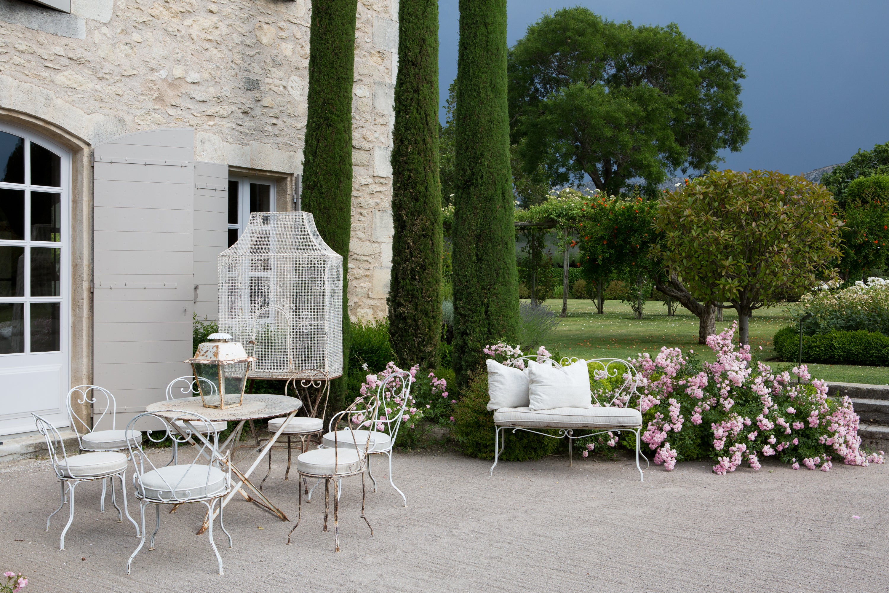 Outdoor patio setting with white furniture and floral decorations in a garden — editorial photography by Carla Coulson