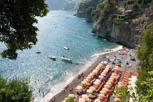Rows of orange and white umbrellas at the Arienzo beach club on the Amalfi Coast with Positano in the background