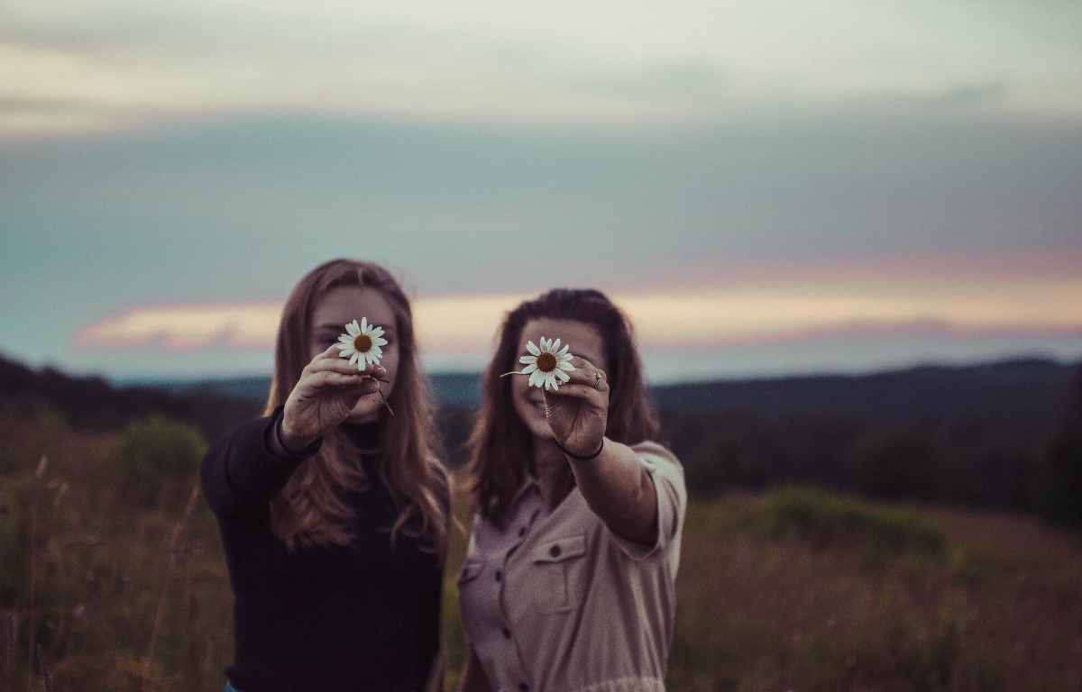 Image of friendship two girls holding daisies in the country 